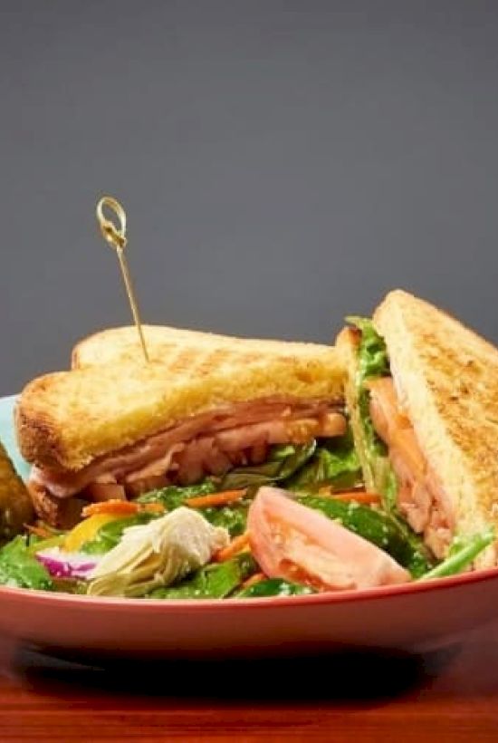 A plate with a stacked club sandwich, toothpicks, and salad on the side; crisp toast, greens, and deli fillings.