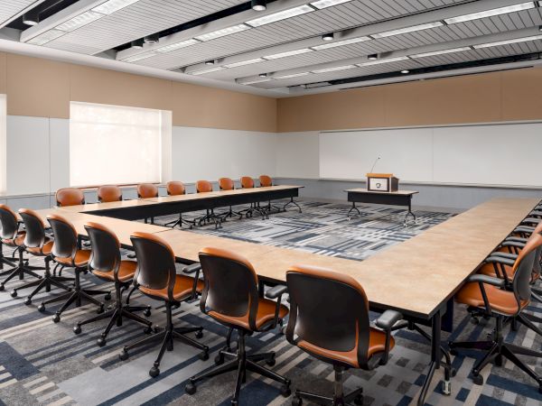 A large conference room with U-shaped table, orange chairs, a projector screen at the front, and whiteboards along the back wall. End sentence.
