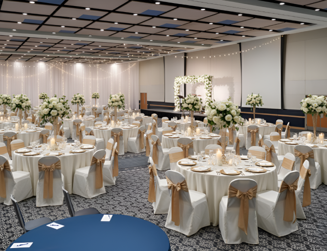 A banquet hall with round tables dressed in white linens, gold sashes, and tall floral centerpieces, arranged for a formal event with elegant settings.